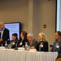 Moderator Dave Mengebier at podium and panel seated at table.
